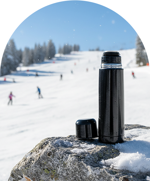 En svart termos på en snötäckt sten, med en skidbacke i bakgrunden.